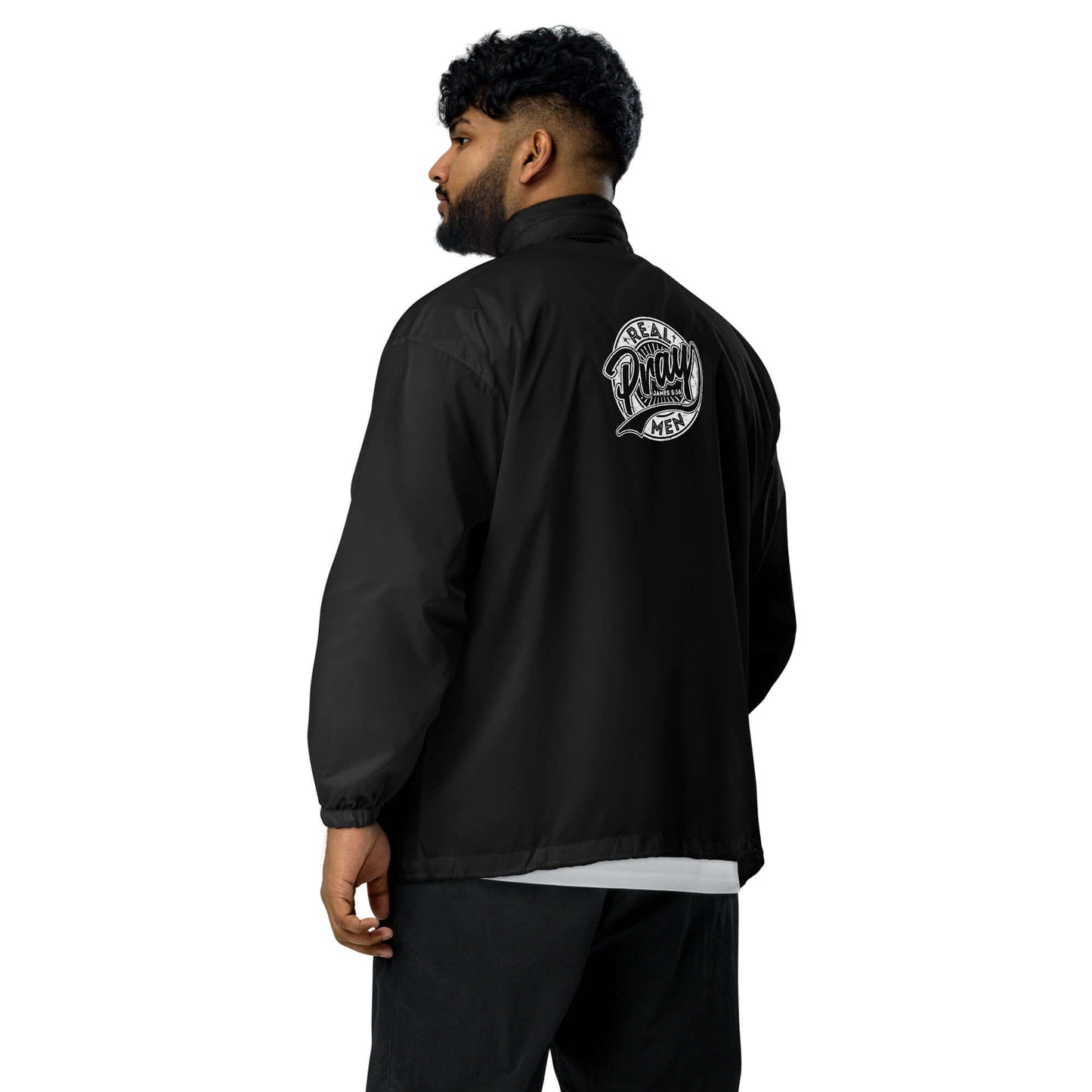 Man wearing a black Real Men Pray windbreaker, showcasing its back design, symbolizing faith and devotion.