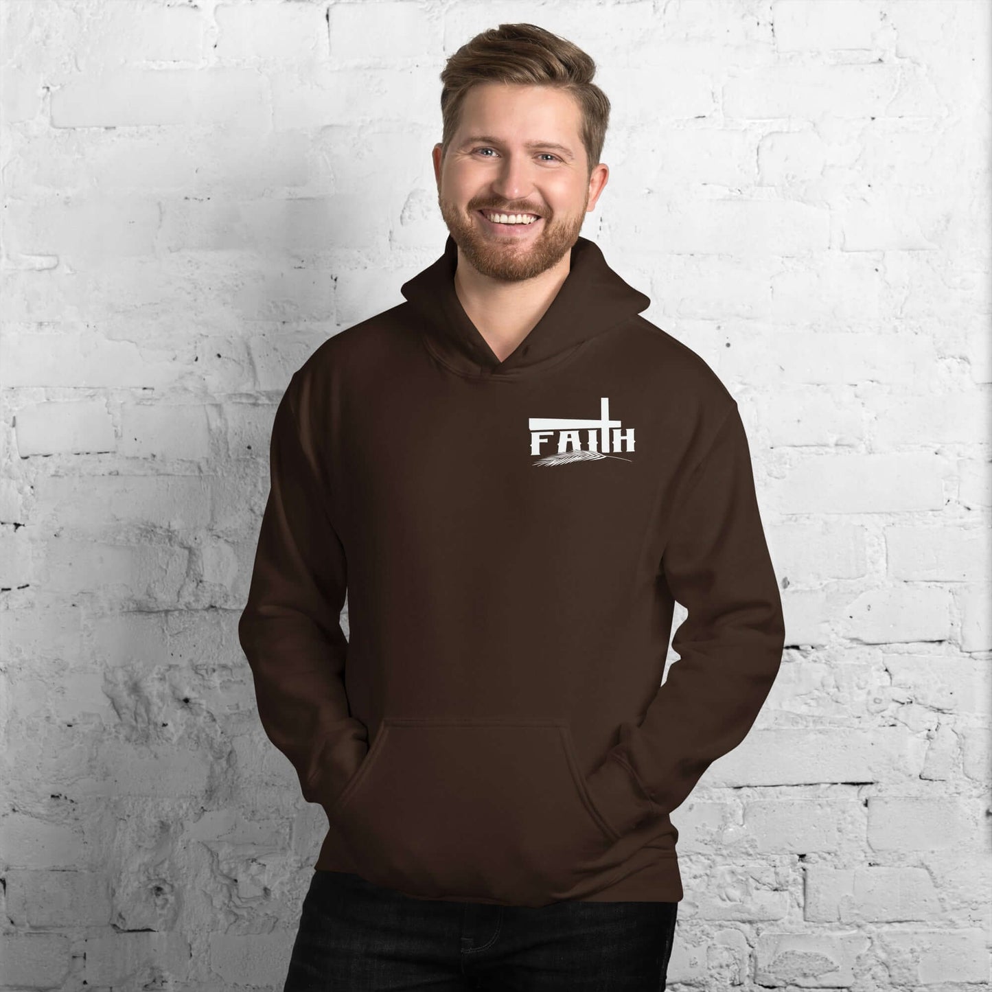 Smiling man wearing a brown 'Faith' hoodie with cross and feather design, inspired by Hebrews 11:1, against a white brick background.