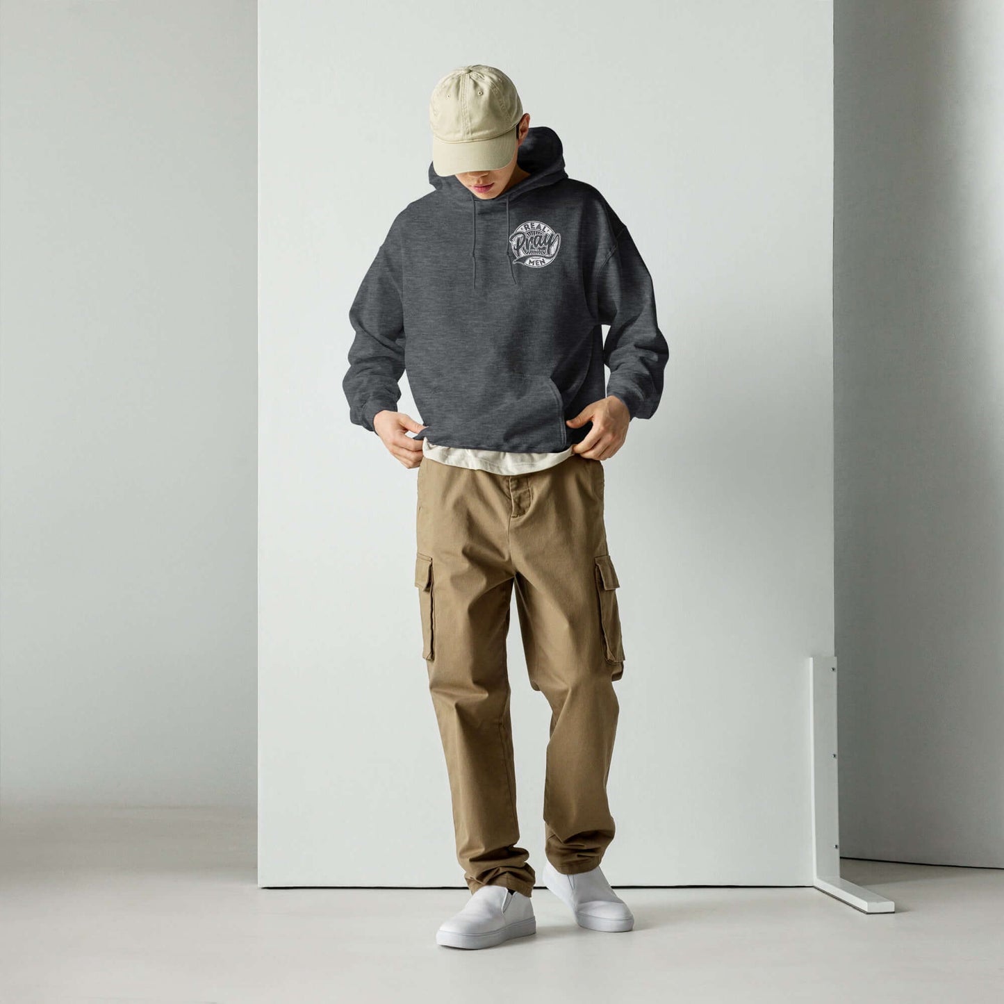 Model wearing a grey "Real Men Pray" hoodie and beige cargo pants, showcasing Christian clothing style in the UK.