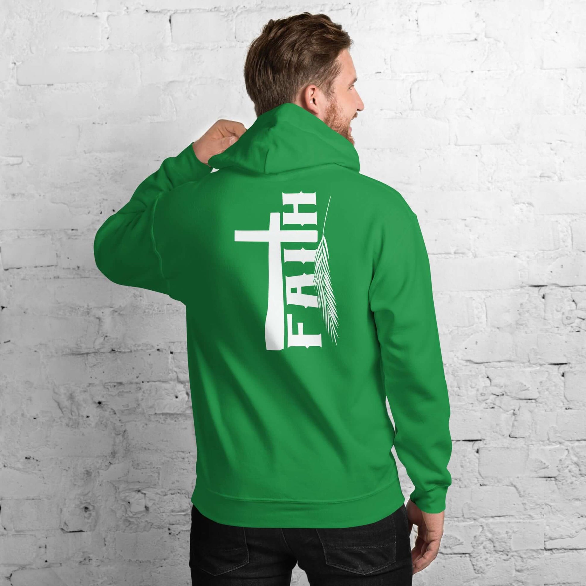 Man in green hoodie with 'Faith' and cross design, inspired by Hebrews 11:1, white brick background, Christian clothing UK.