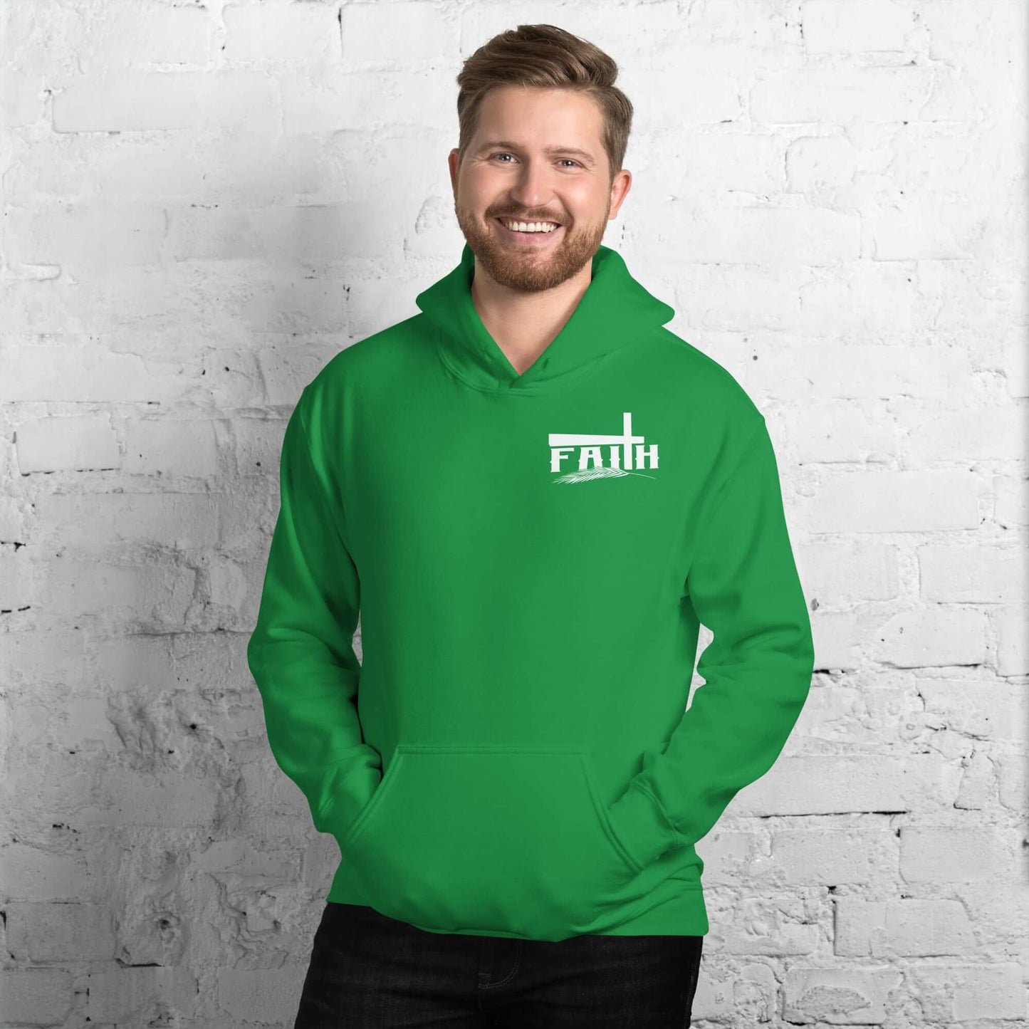 Smiling man wearing a green Faith hoodie with cross and feather design, inspired by Hebrews 11:1, against a white brick background