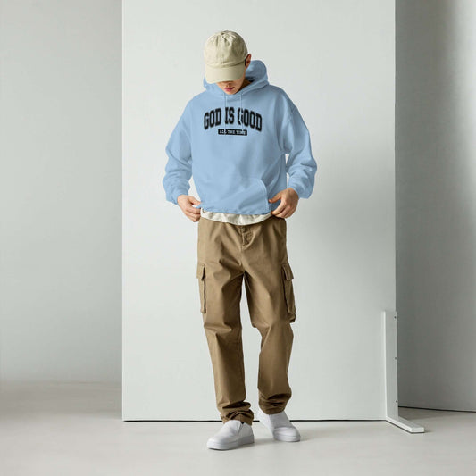 Light blue "God is Good" unisex hoodie worn with beige cargo pants, representing Christian clothing style in the UK.