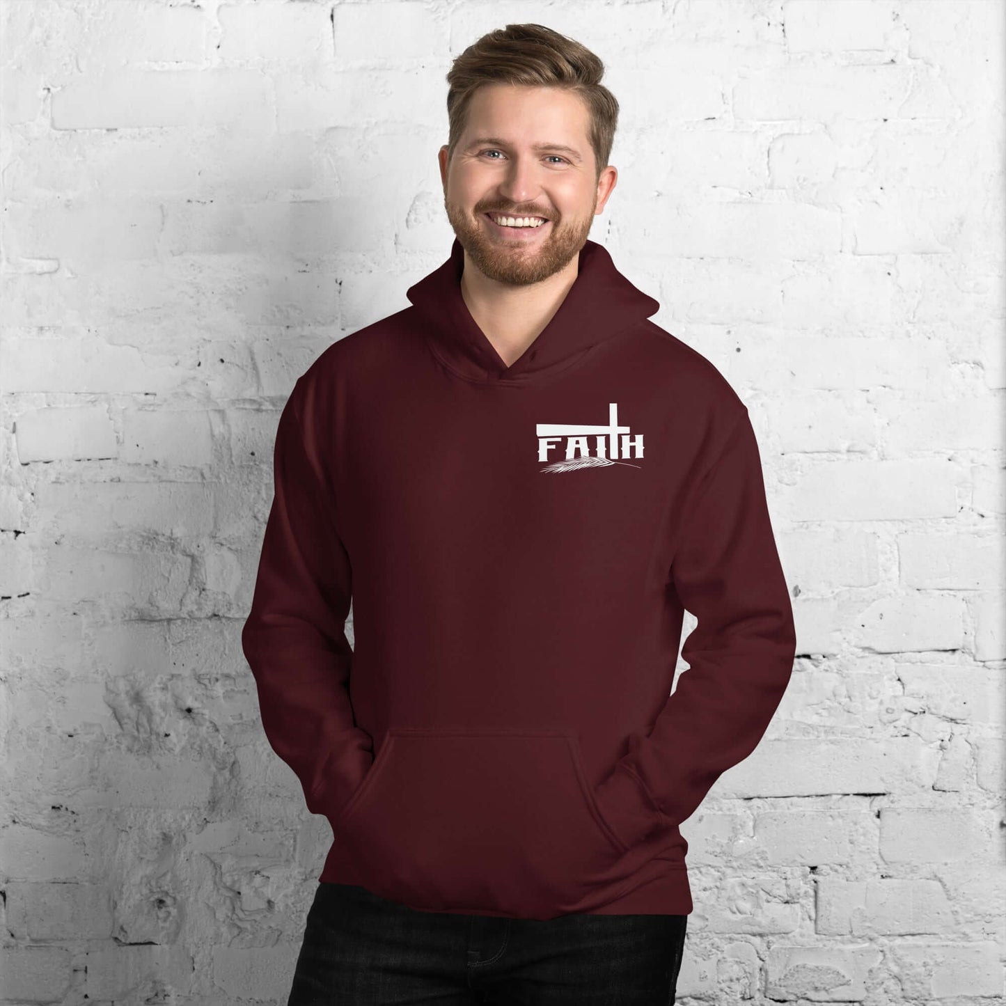 Man smiling wearing a maroon Faith Hoodie with cross and feather design, inspired by Hebrews 11:1, against a white brick background, Christian clothing UK.