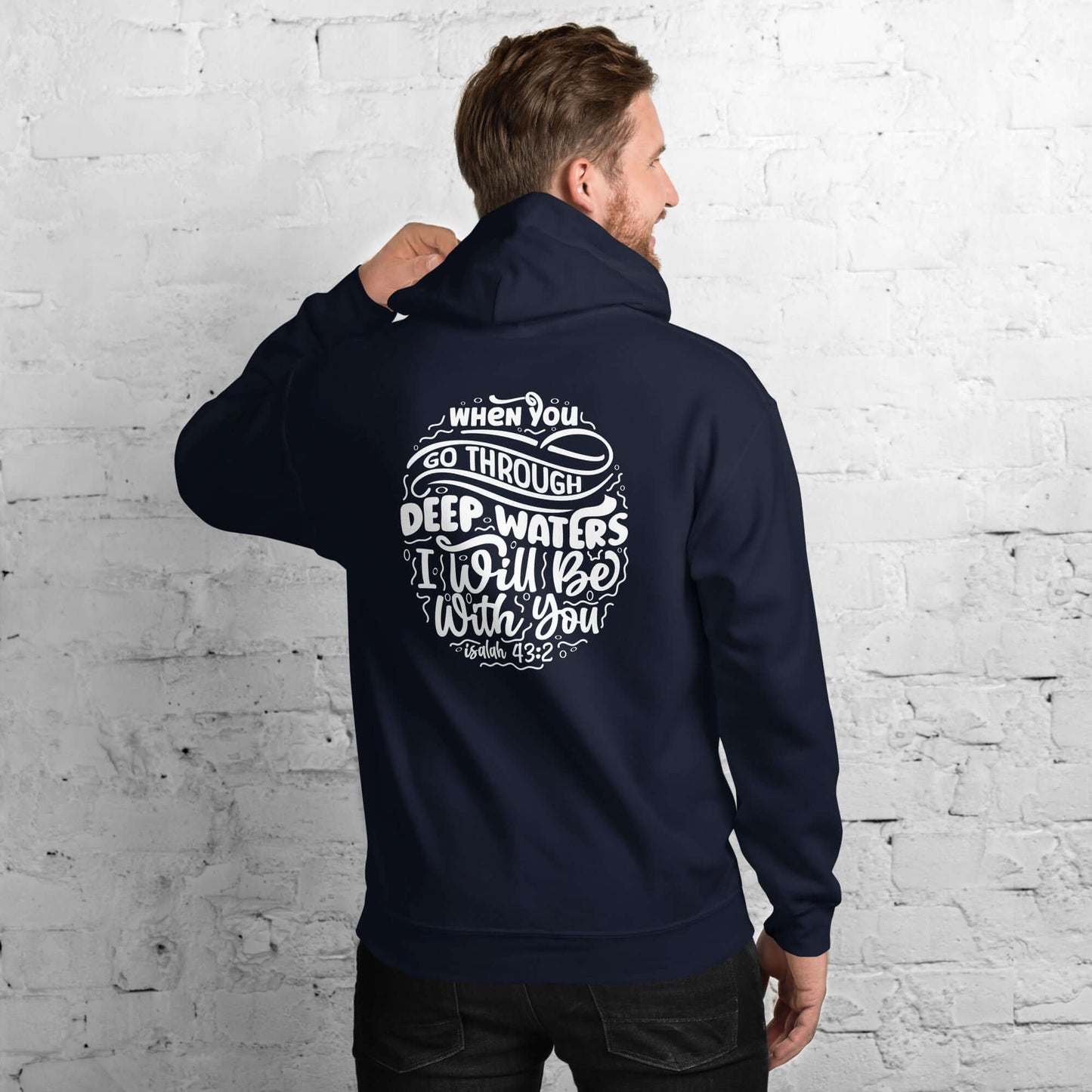 Man wearing a blue 'Through Deep Waters' hoodie inspired by Isaiah 43:2, Christian clothing UK, back view against a white brick wall.