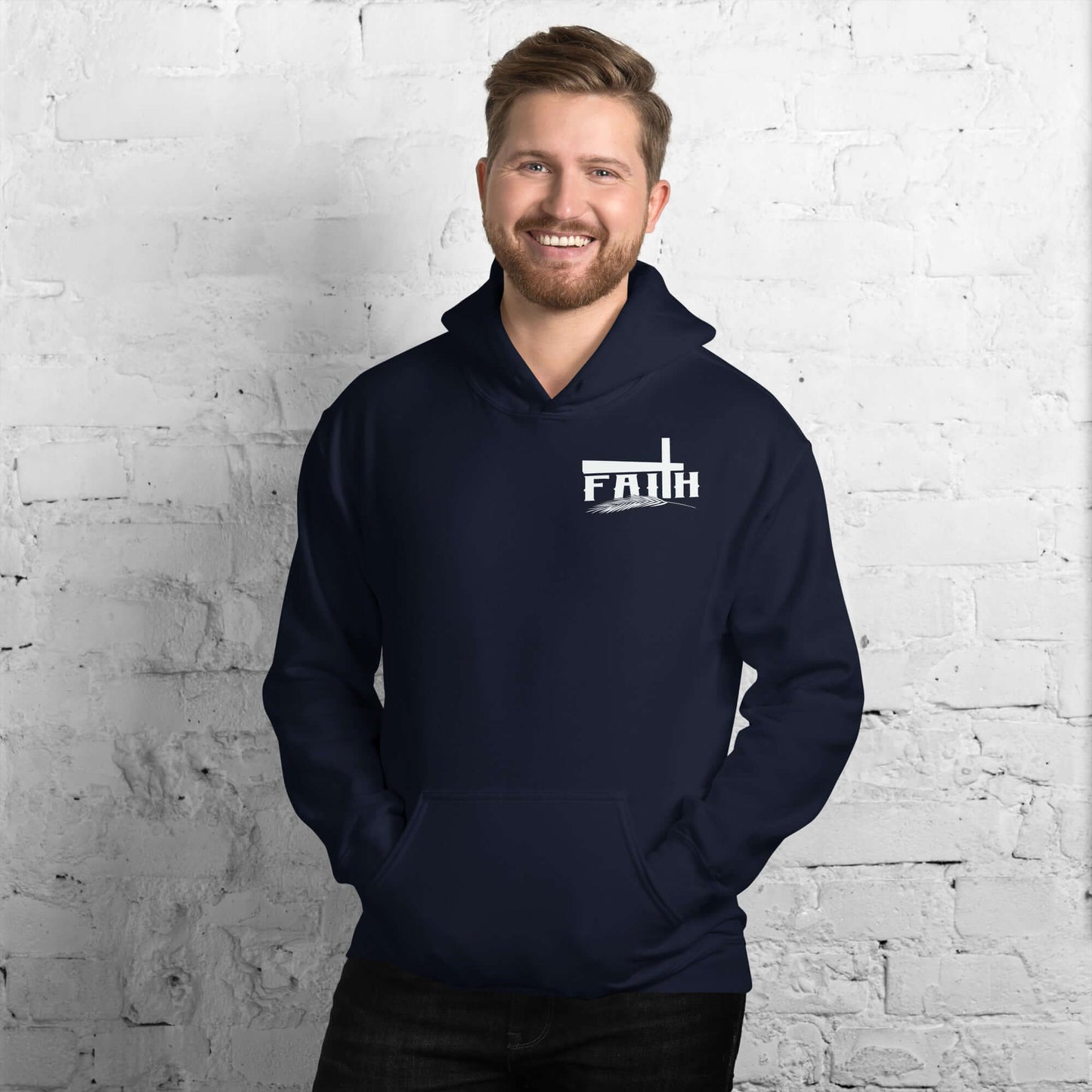 Smiling man wearing a navy blue Faith hoodie with cross and feather design, inspired by Hebrews 11:1, against a white brick background.