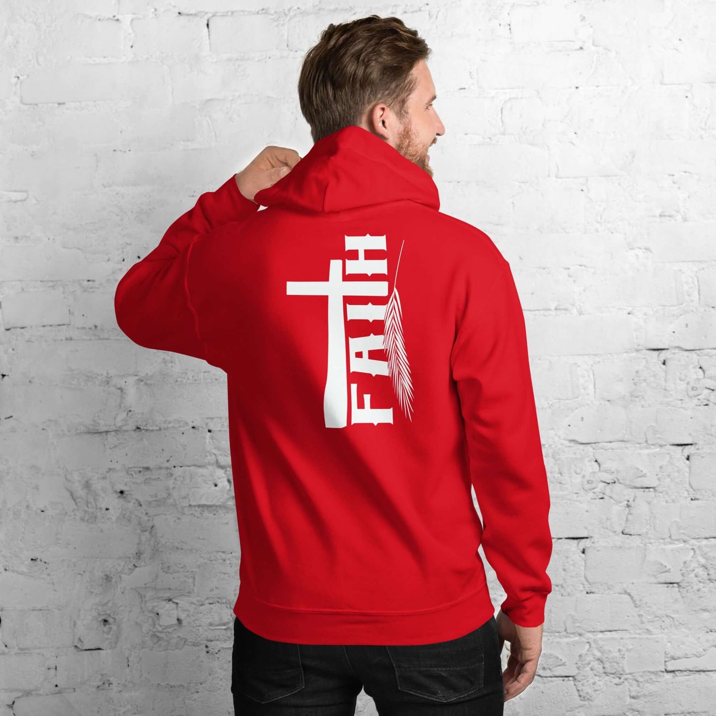 Man wearing red Faith hoodie with cross and feather design, inspired by Hebrews 11:1, against a white brick background; Christian clothing UK.