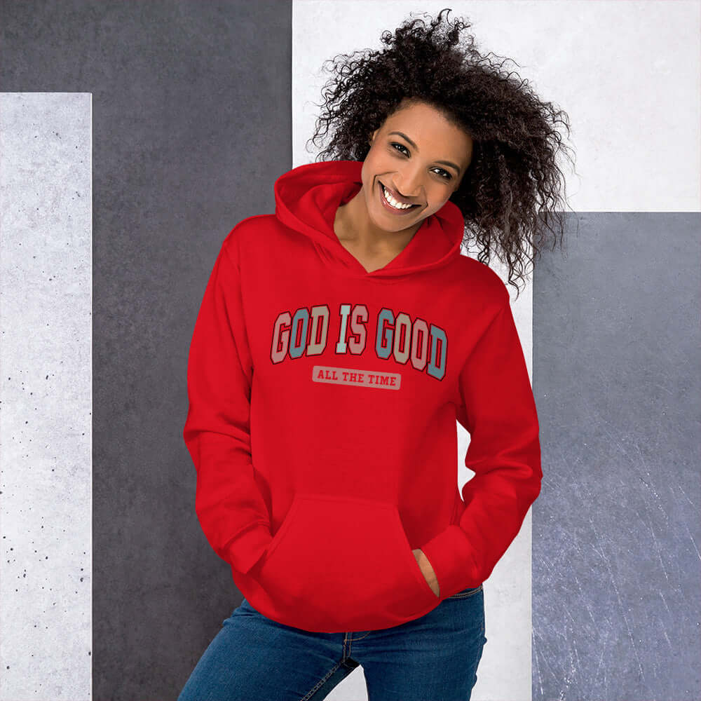 Woman wearing a red "God is Good" hoodie, showcasing cheerful Christian clothing in a trendy design, ideal for casual wear.