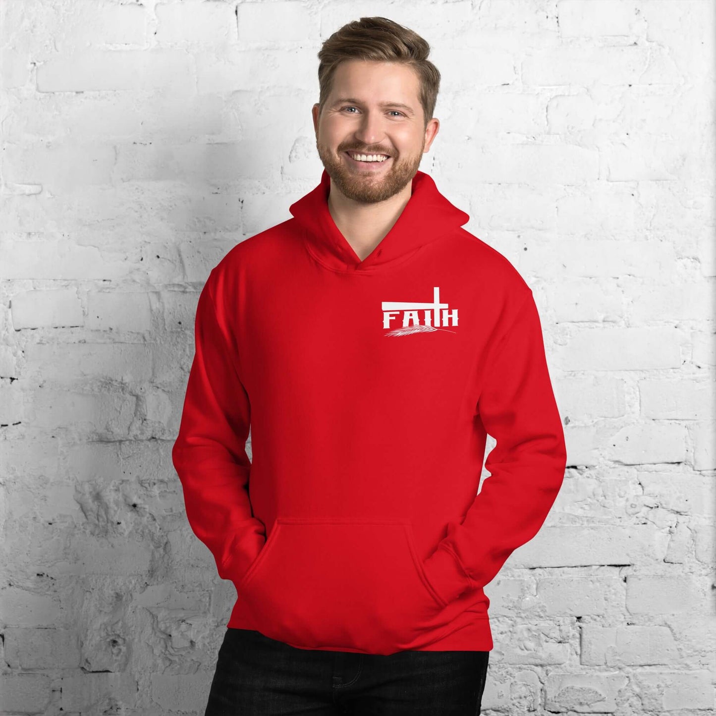 Smiling man wearing a red 'Faith' hoodie with cross and feather design, inspired by Hebrews 11:1, against a white brick background, Christian clothing UK.