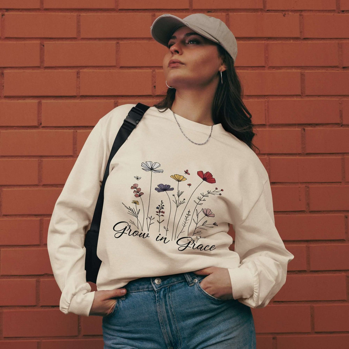 Woman wearing "Grow in Grace" Christian sweatshirt with floral design, standing against a brick wall.