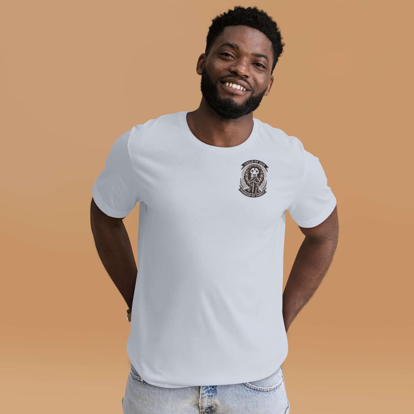 Smiling man wearing a white Christian T-shirt with 'Child of God, Warrior of Christ' emblem, inspired by Ephesians 6:10-11, against a soft orange background.