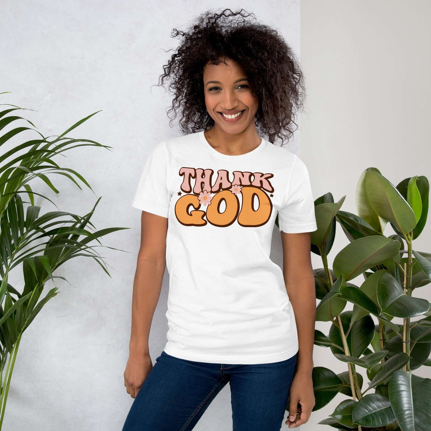 Woman wearing a "Thank God" Christian T-shirt with modern typography, surrounded by plants.